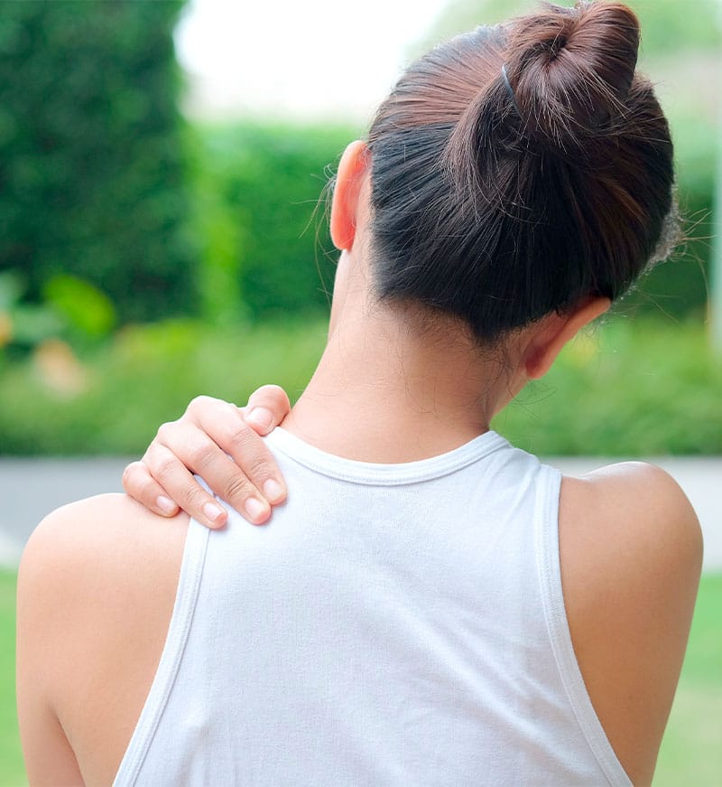 A person holds their shoulder, indicating discomfort or pain in the upper back area - Pain Management