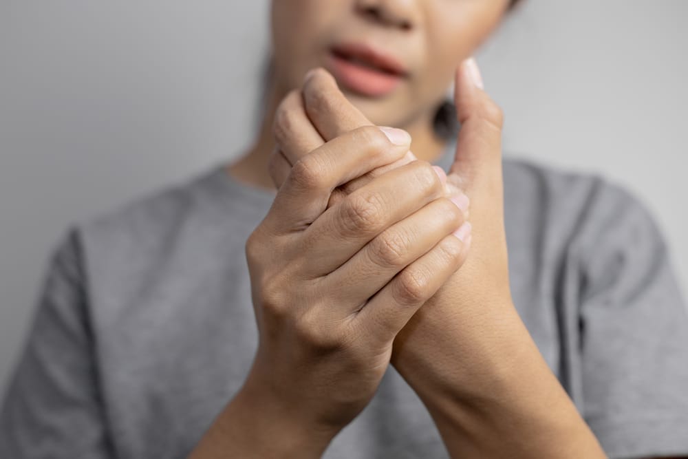 A person holds their hand, appearing to massage or relieve discomfort in their fingers - Chiropractor Kennesaw GA A person holds their hand, appearing to massage or relieve discomfort in their fingers - Chiropractor Kennesaw GA